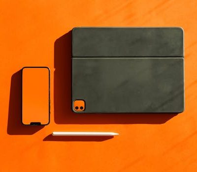 Stylish flat lay of digital devices and stylus on a vibrant orange surface, ideal for technology themes.